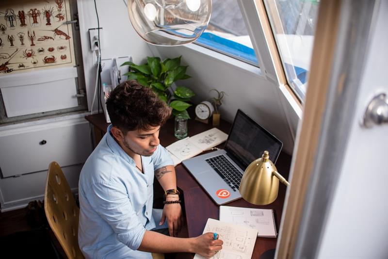 man at desk next to laptop taking notes