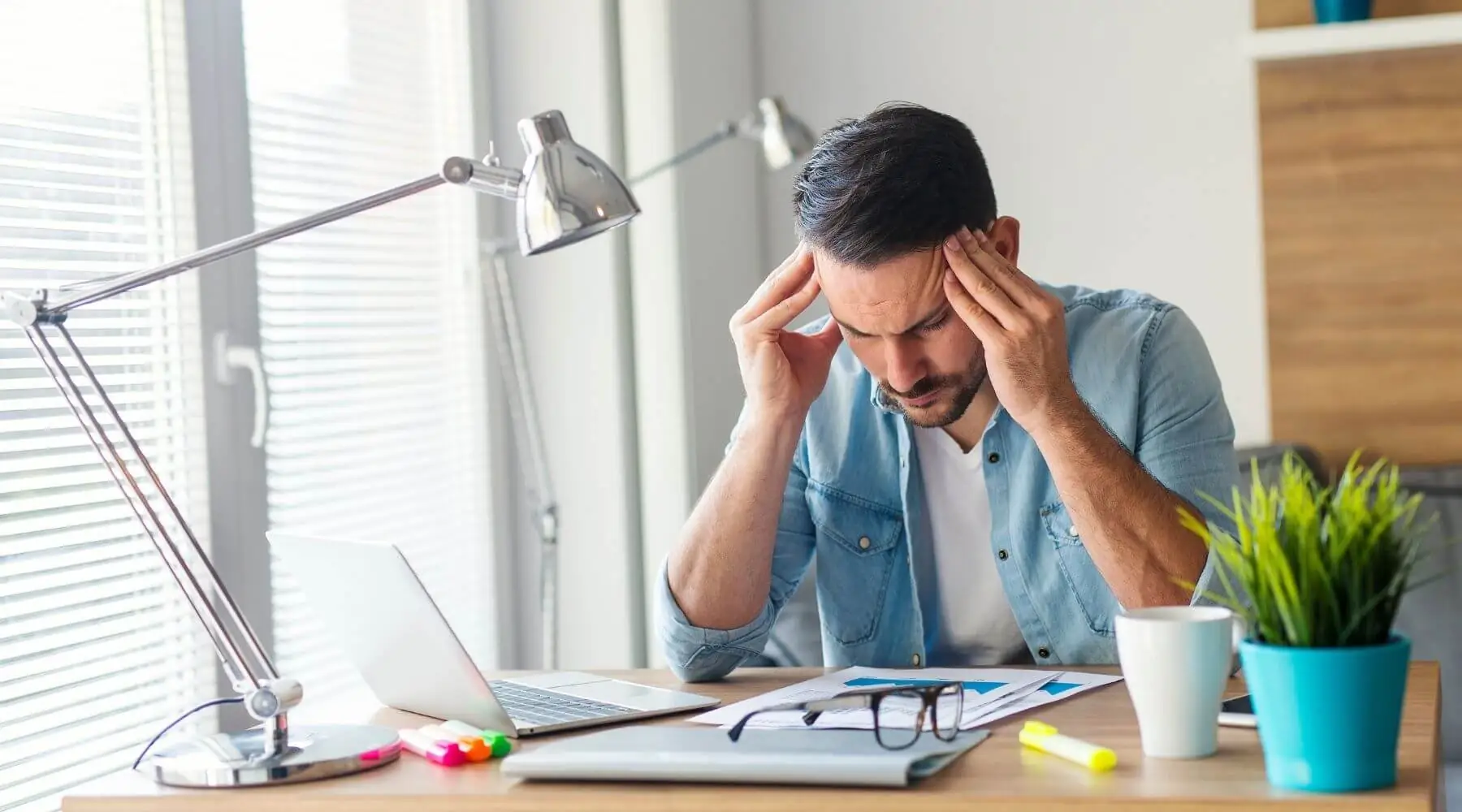 Male at desk holding head