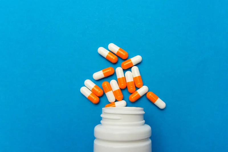Orange white capsules (pills) were poured from a white bottle on a blue background. Medical background, template.